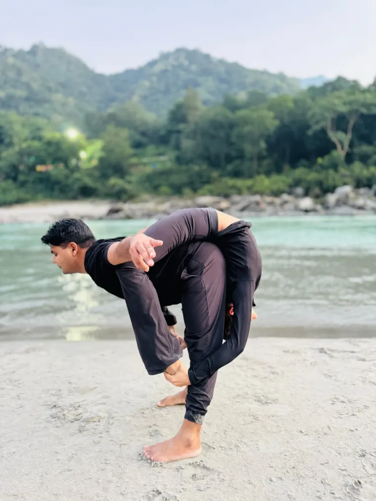 A standing acro yoga base carrying a partner across his back on the sand beside the Ganga in Rishikesh