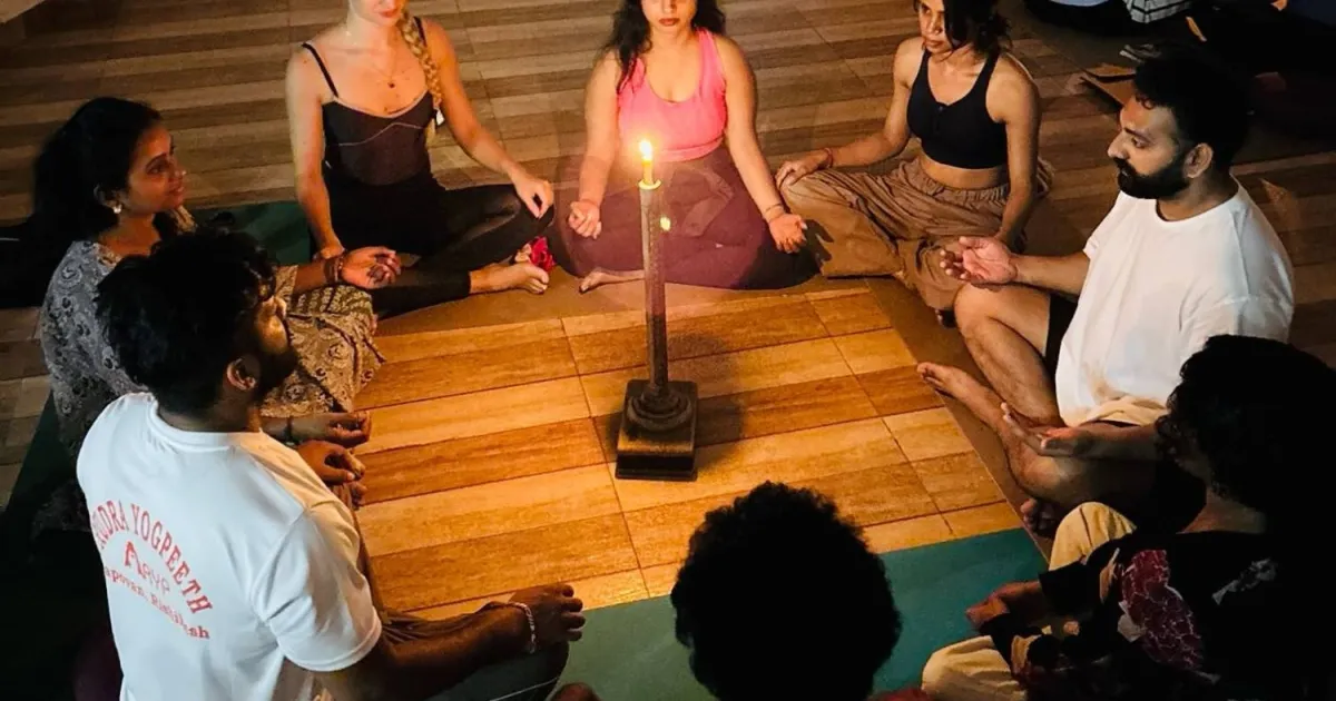 Students sitting in a circle around a candle during an evening meditation session at Rudra Yogpeeth in Rishikesh