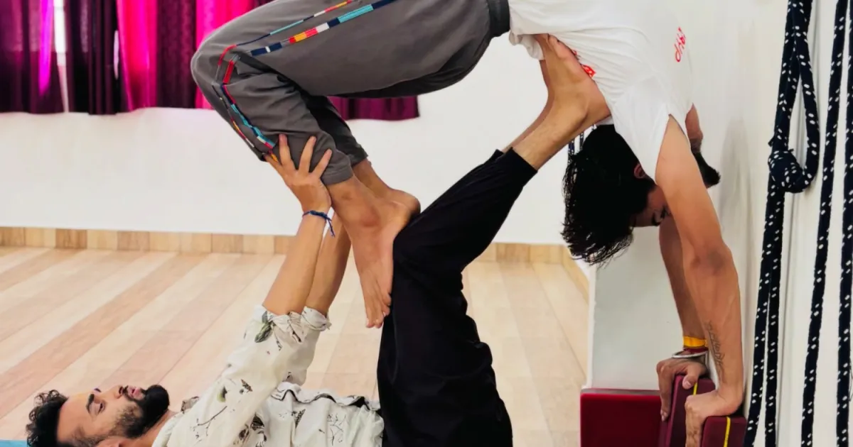 A supported partner backbend being practised with blocks and wall ropes in the shala at Rudra Yogpeeth in Rishikesh