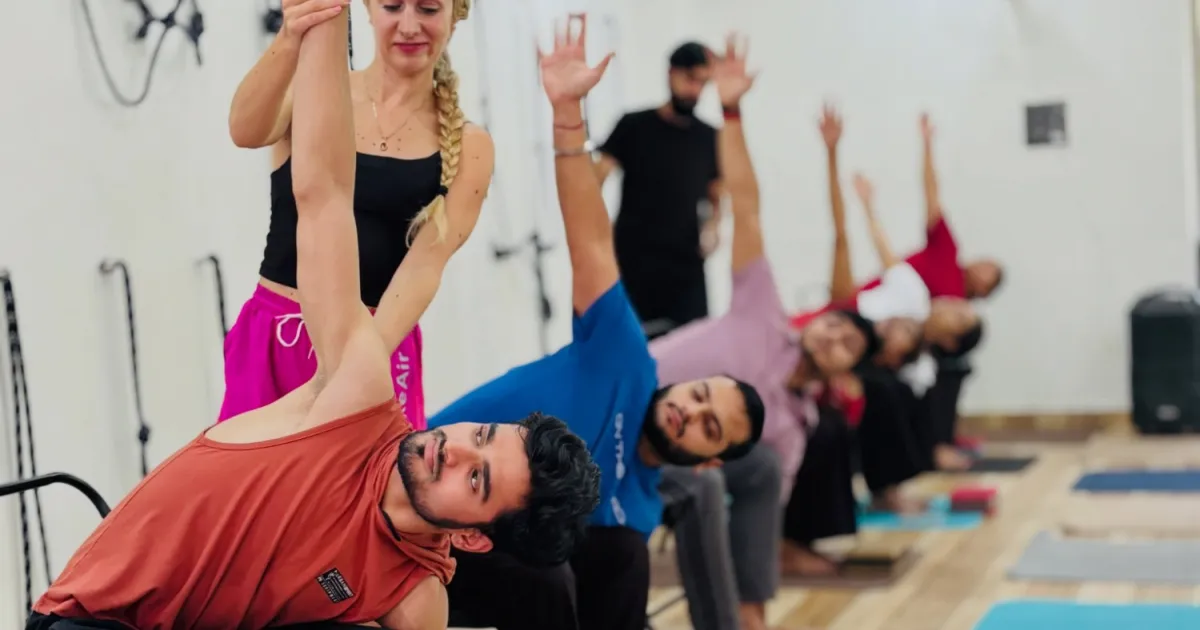 A teacher guiding a row of students through a seated side stretch during a class at Rudra Yogpeeth in Rishikesh