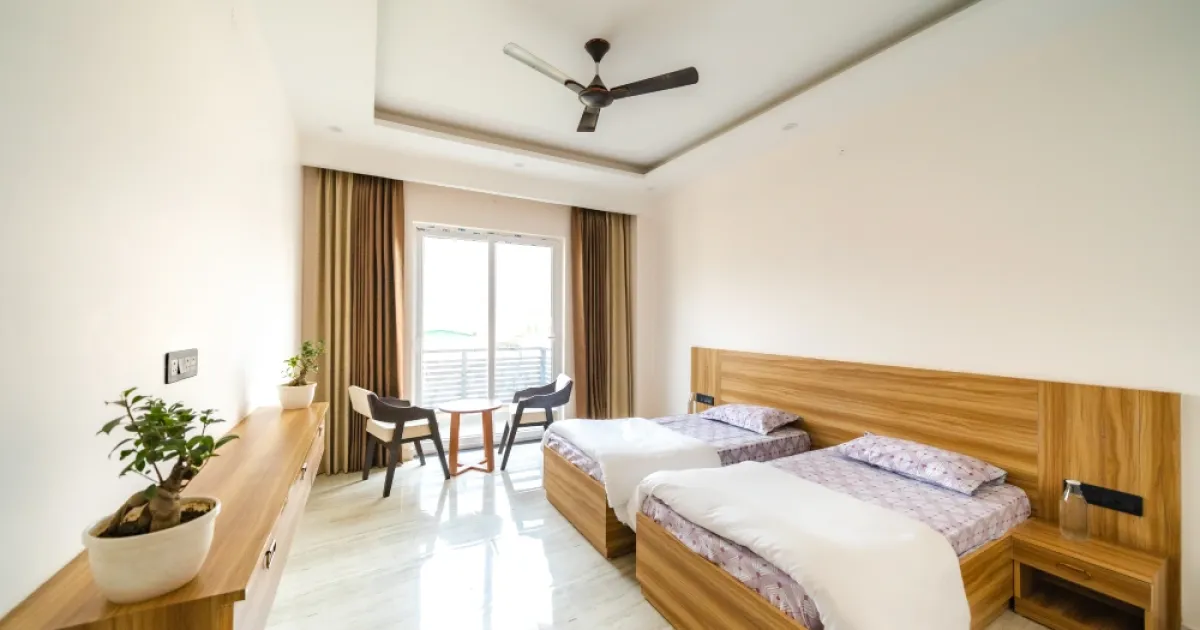 A twin room at Rudra Yogpeeth in Rishikesh with two beds, a balcony and a study table