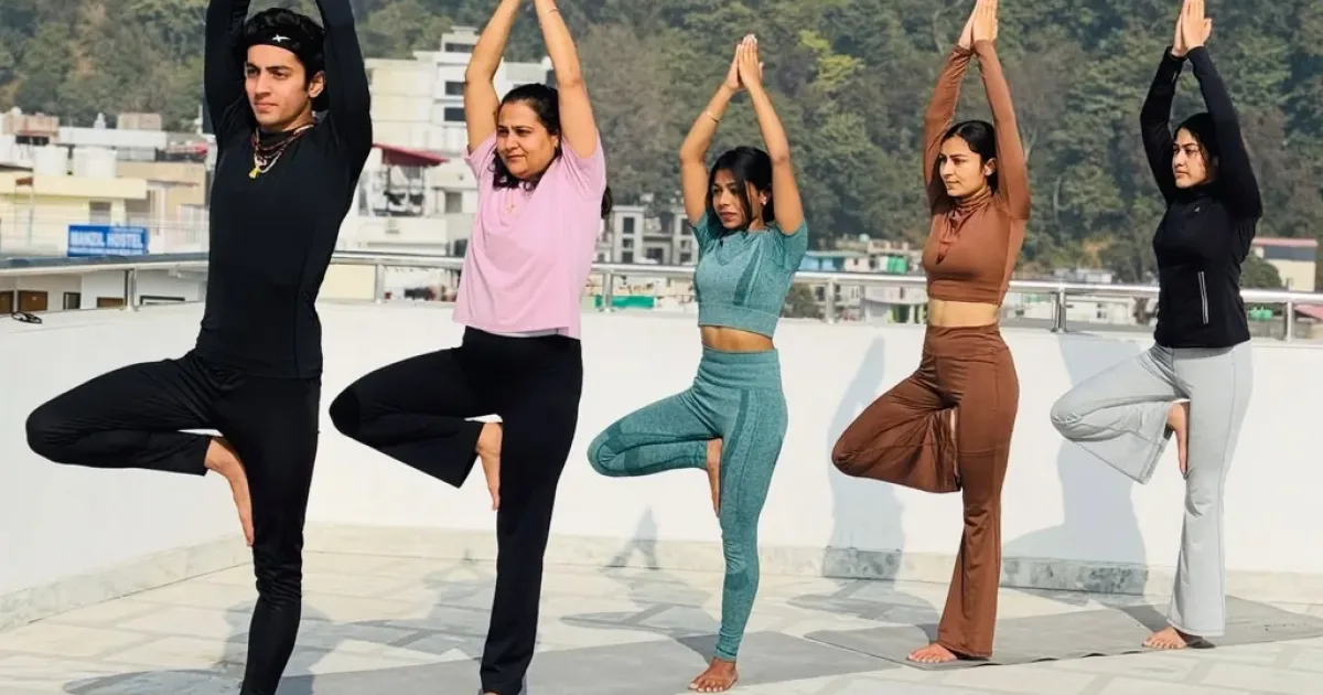 A mixed-level yoga class practising tree pose on the Rudra Yogpeeth rooftop in Rishikesh
