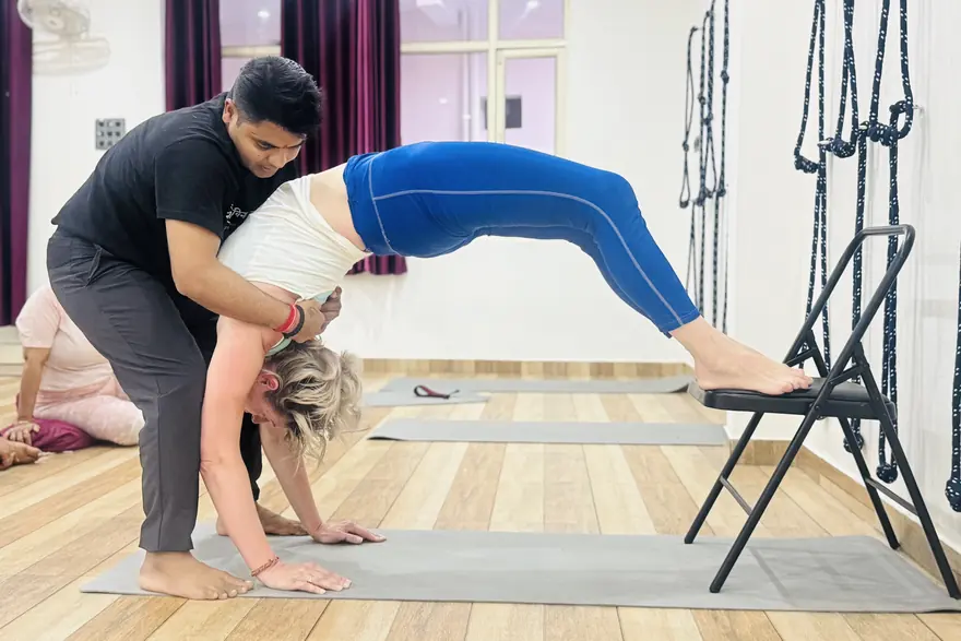 A teacher guiding a student through a supported backbend at Rudra Yogpeeth
