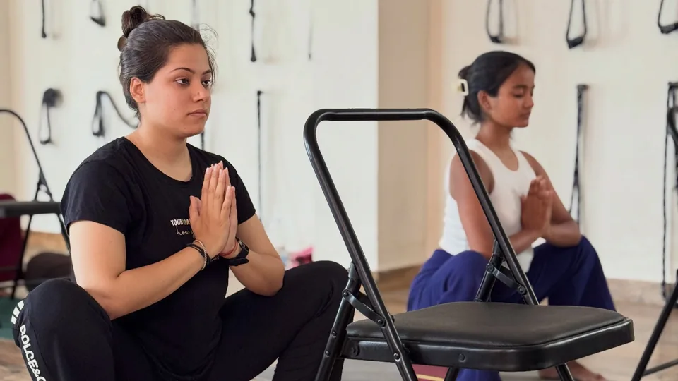 Pregnant student in a supported squat with hands at the heart during prenatal yoga training