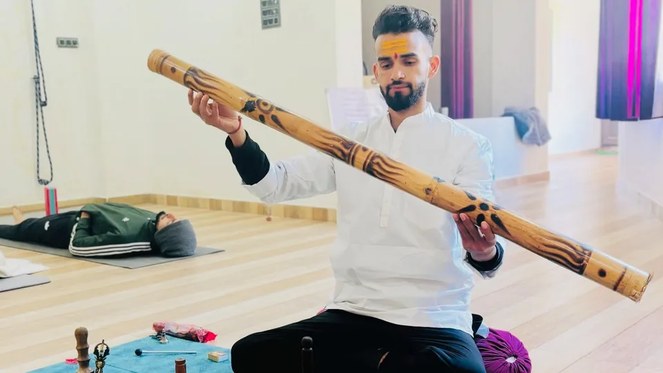 Sound healing teacher playing a didgeridoo beside singing bowls and gongs at Rudra Yogpeeth, Rishikesh
